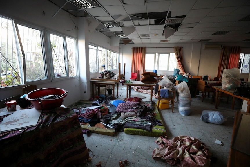 The interior of a building with belongings strewn around, broken windows and a damaged ceiling. 