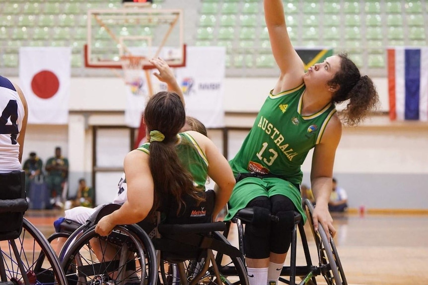 Annabelle Lindsay reaches for a basketball ball while sitting in a wheelchair