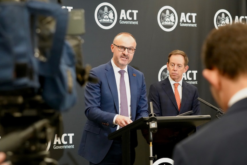 Andrew Barr stands behind a lectern speaking to people, with Attorney-General Shane Rattenbury behind him.