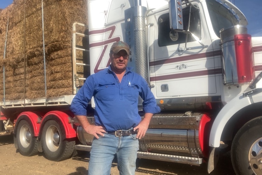 A farmer stands in front of a truck loaded with hay.