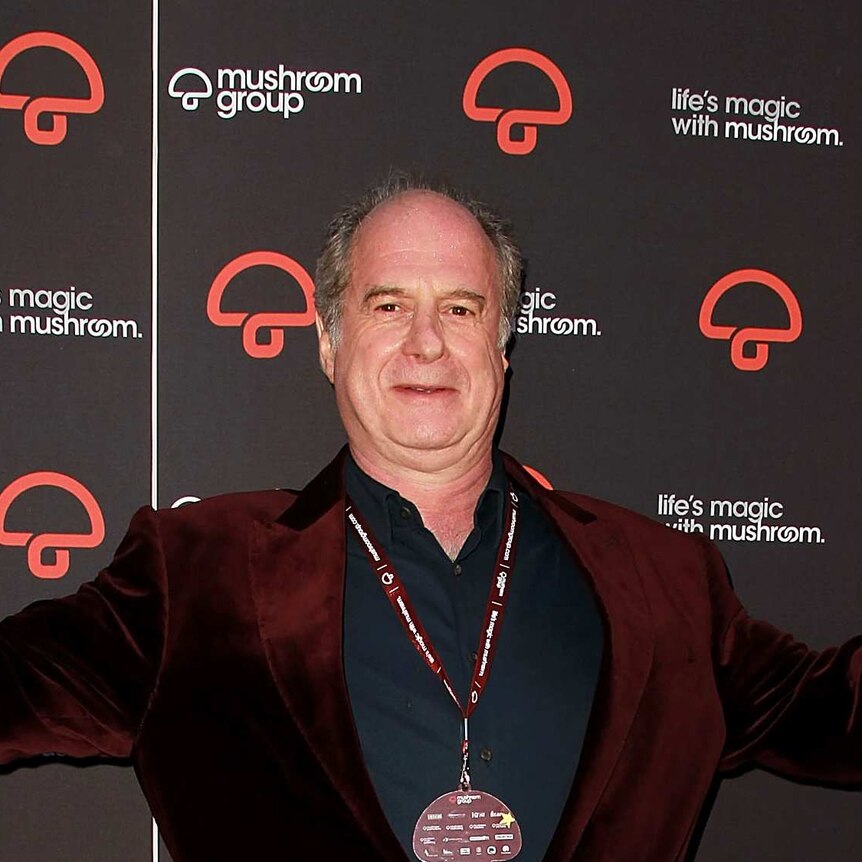 Michael Gudinski with his hands in the air starting in front of a Mushroom Group sign