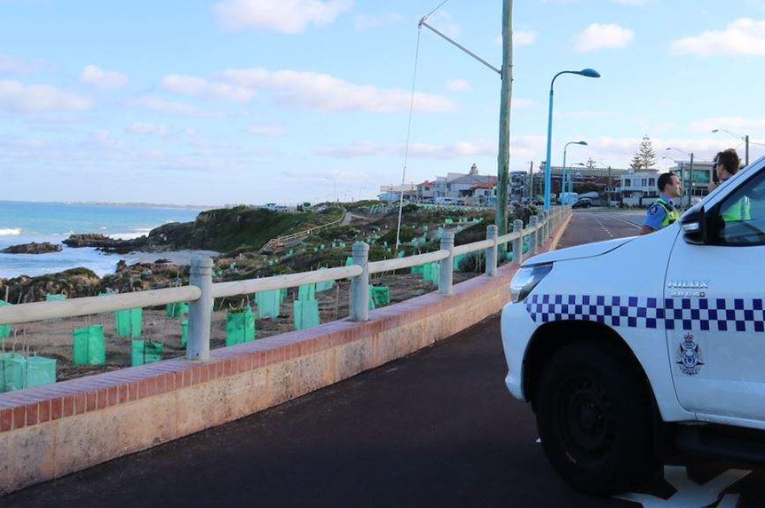 A police officer near a police car parked across a cycle path at Trigg Beach.