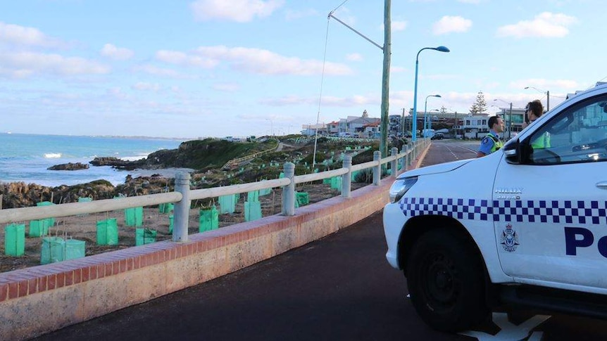 A police officer near a police car parked across a cycle path at Trigg Beach.