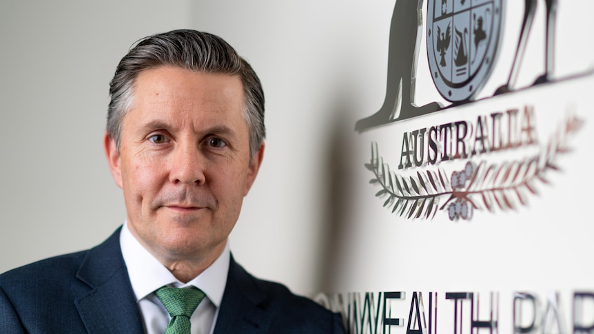 A man wearing a suit and tie next to a sign saying AUSTRALIA