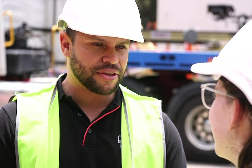 a man wearing a hard hat talking to a young woman wearing glasses