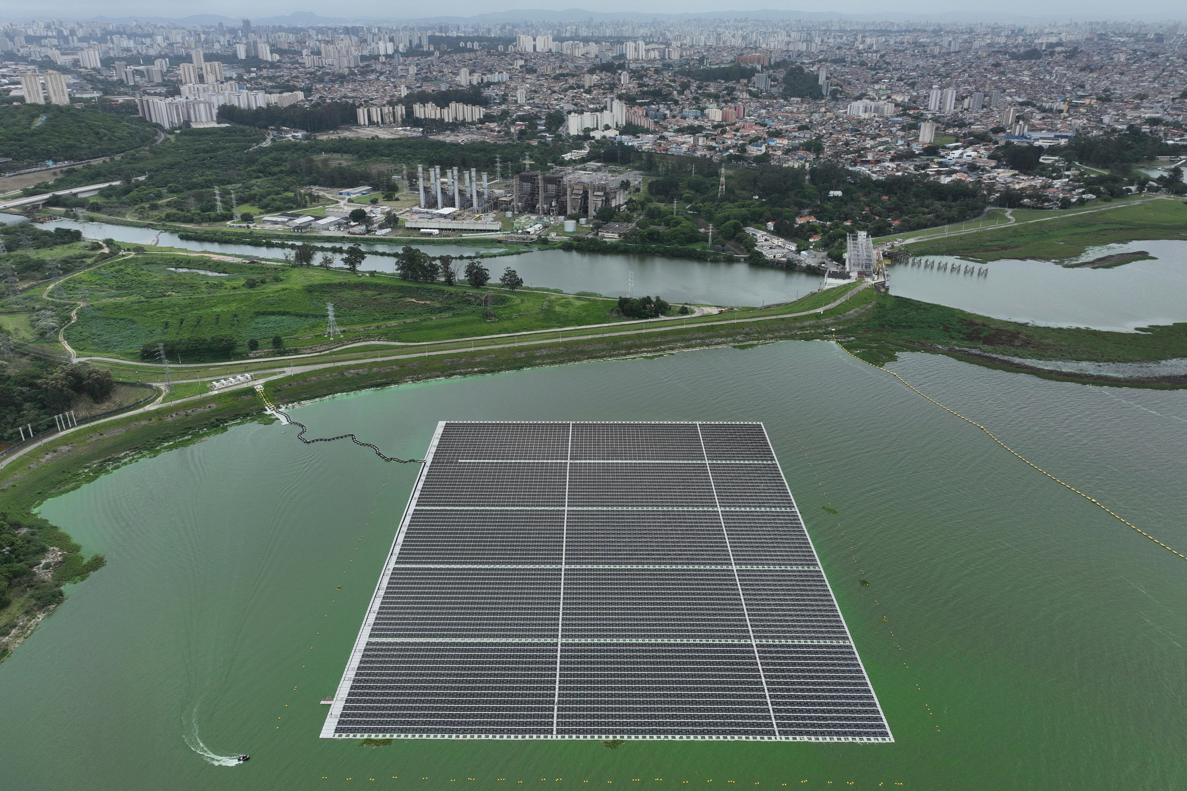 A large floating array of solar panels floating on a waterbody with a city seen in the background.