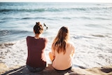 Two young women sitting on a rock by the ocean to depict how to make and keep friends after leaving high school.