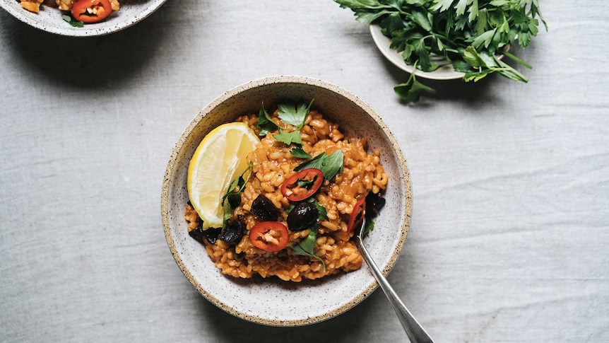 A bowl of puttanesca risotto topped with parsley, sliced chilli and a lemon wedge, a fuss free family dinner.