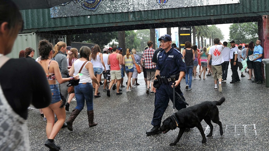 A police officer with a dog walks near young people.