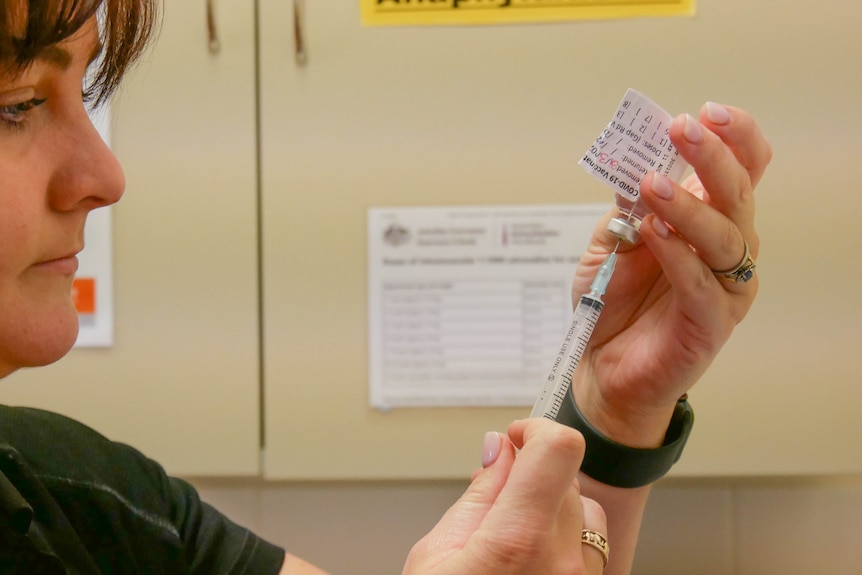 A woman holds a syringe and a small vial, and extracts the COVID-19 vaccine from the vial. 