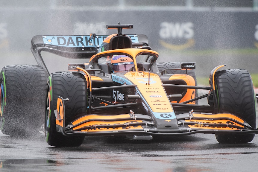 Orange F1 car drives through a corner in wet conditions