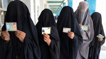 Burqa-clad Afghan women show identification cards as they wait to vote (Banaras Khan/AFP)
