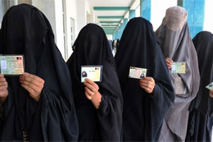 Burqa-clad Afghan women show identification cards as they wait to vote (Banaras Khan/AFP)