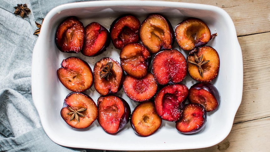 Halved plums in a baking tray with star anise, ready to be roasted.