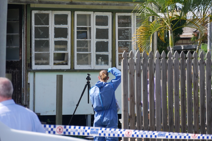 A police officer, wearing blue overalls, takes a photograph of a house 
