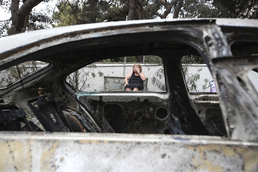 A woman looks on amid burned cars in Mati, Greece