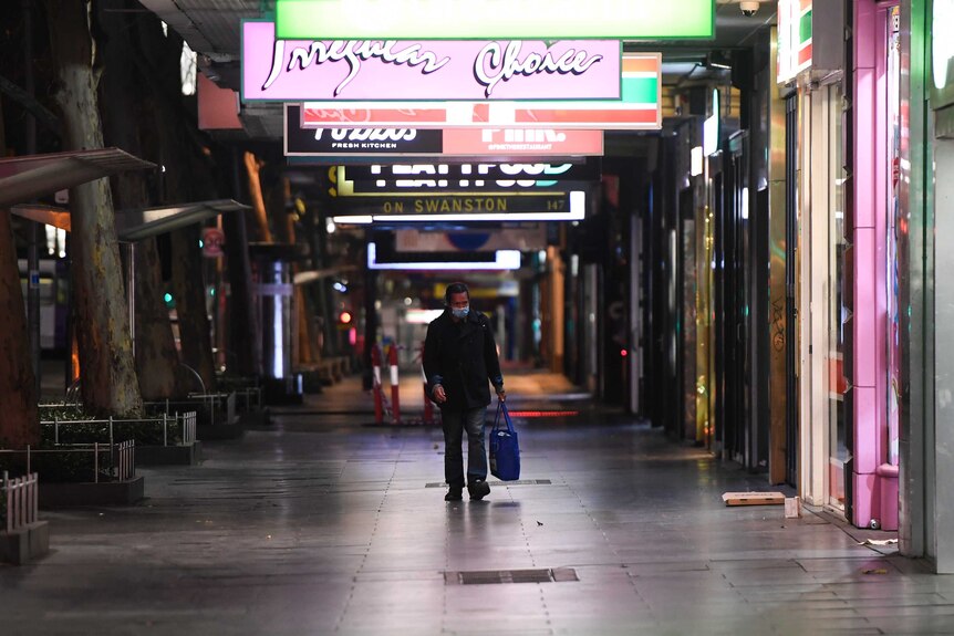 A man walks alone down a street in Melbourne at night-time.