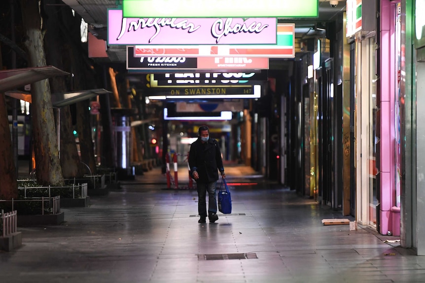 A man walks alone down a street in Melbourne at night-time.