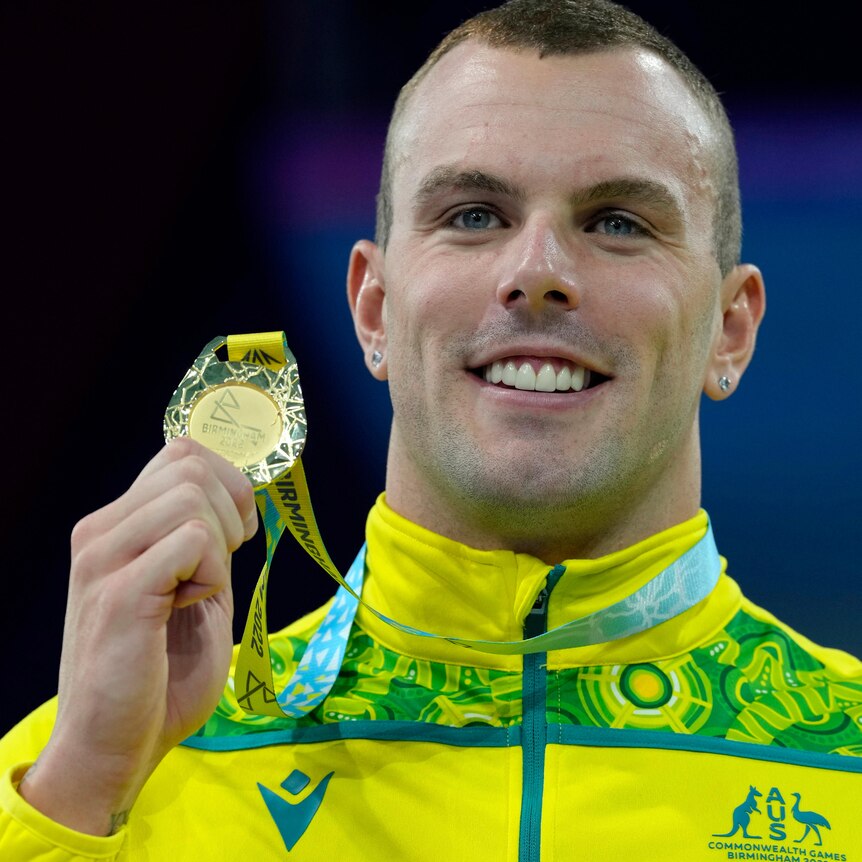 Australian swimmer Kyle Chalmers smiles as he holds his gold medal up on the podium at the Commonwealth Games.