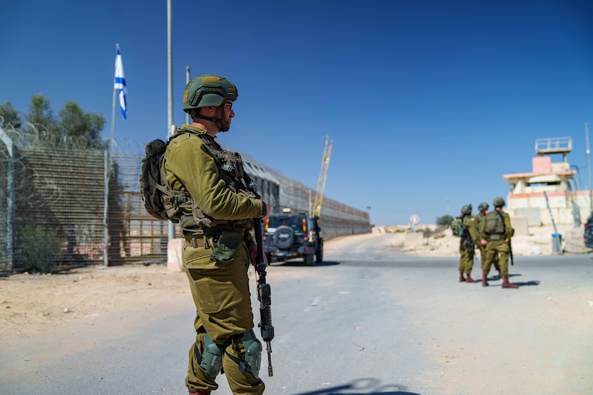 A soldier with a gun as an Israeli flag flutters behind him 