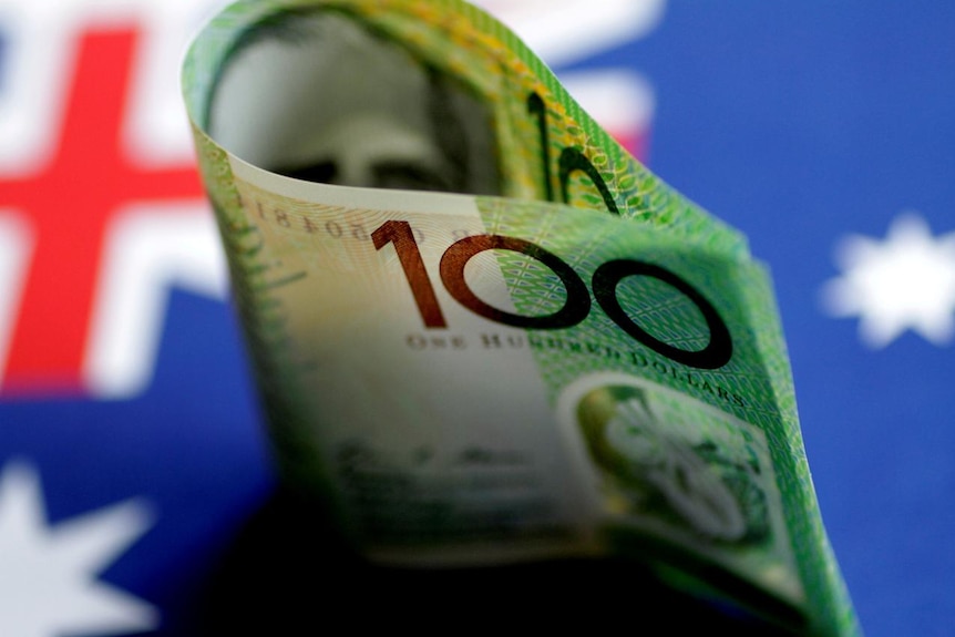 An Australian $100  note is seen with Australian flag behind
