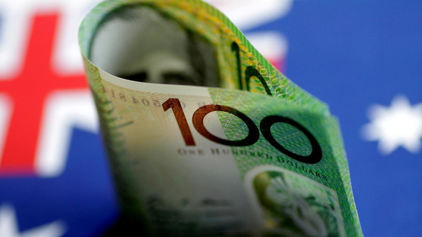 An Australian $100 note is seen with Australian flag behind