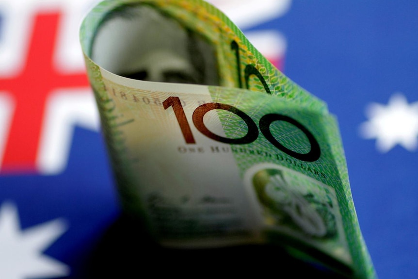 An Australian $100 note is seen with Australian flag behind