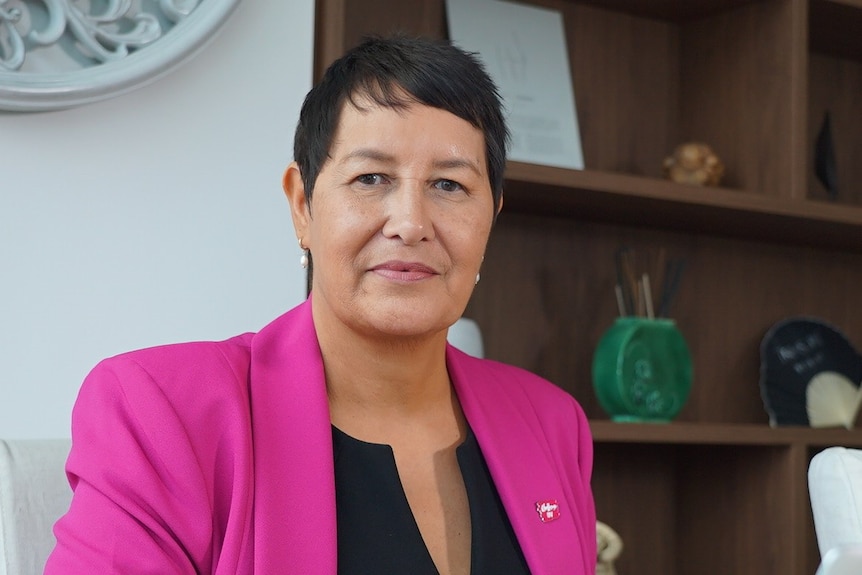 Jacque sitting in her home office in a pink jacket and black top.