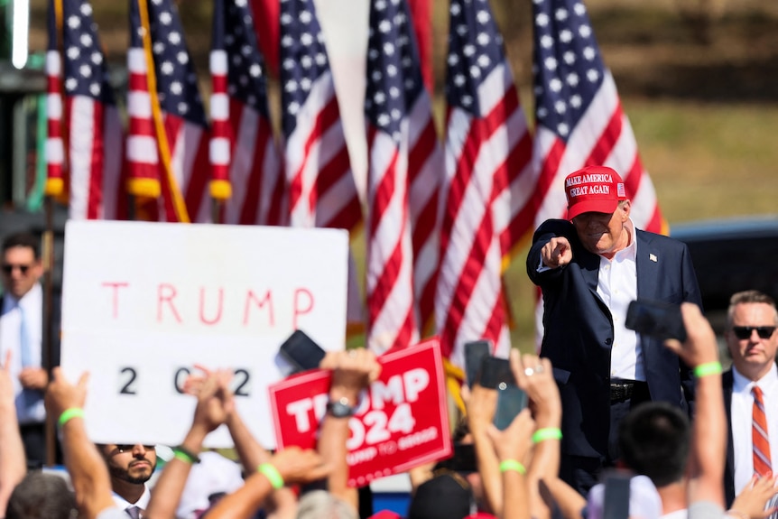 Trump points at a rally with his name on signs and US flags behind him