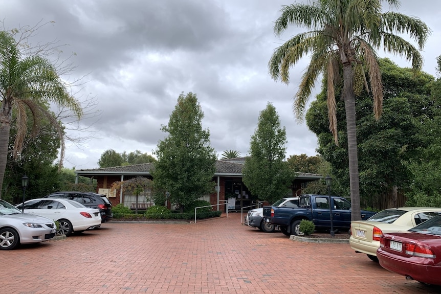 Cars are parked in the brick carpark of an aged care home with a reception building at the back.
