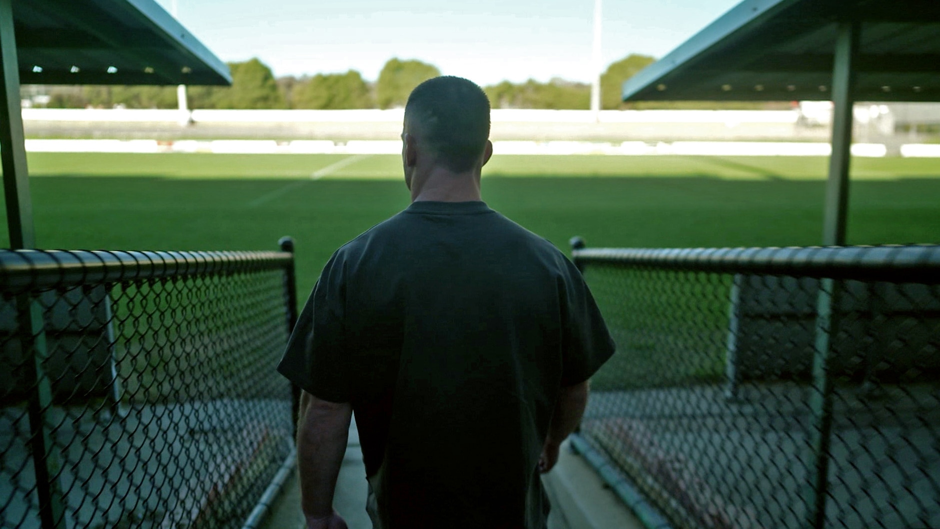 A shot of the back of a man as he walks towards a large green football field.
