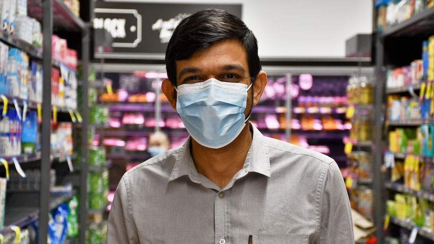 A man in a grey button up shirt stands in the middle of a grocery store aisle.