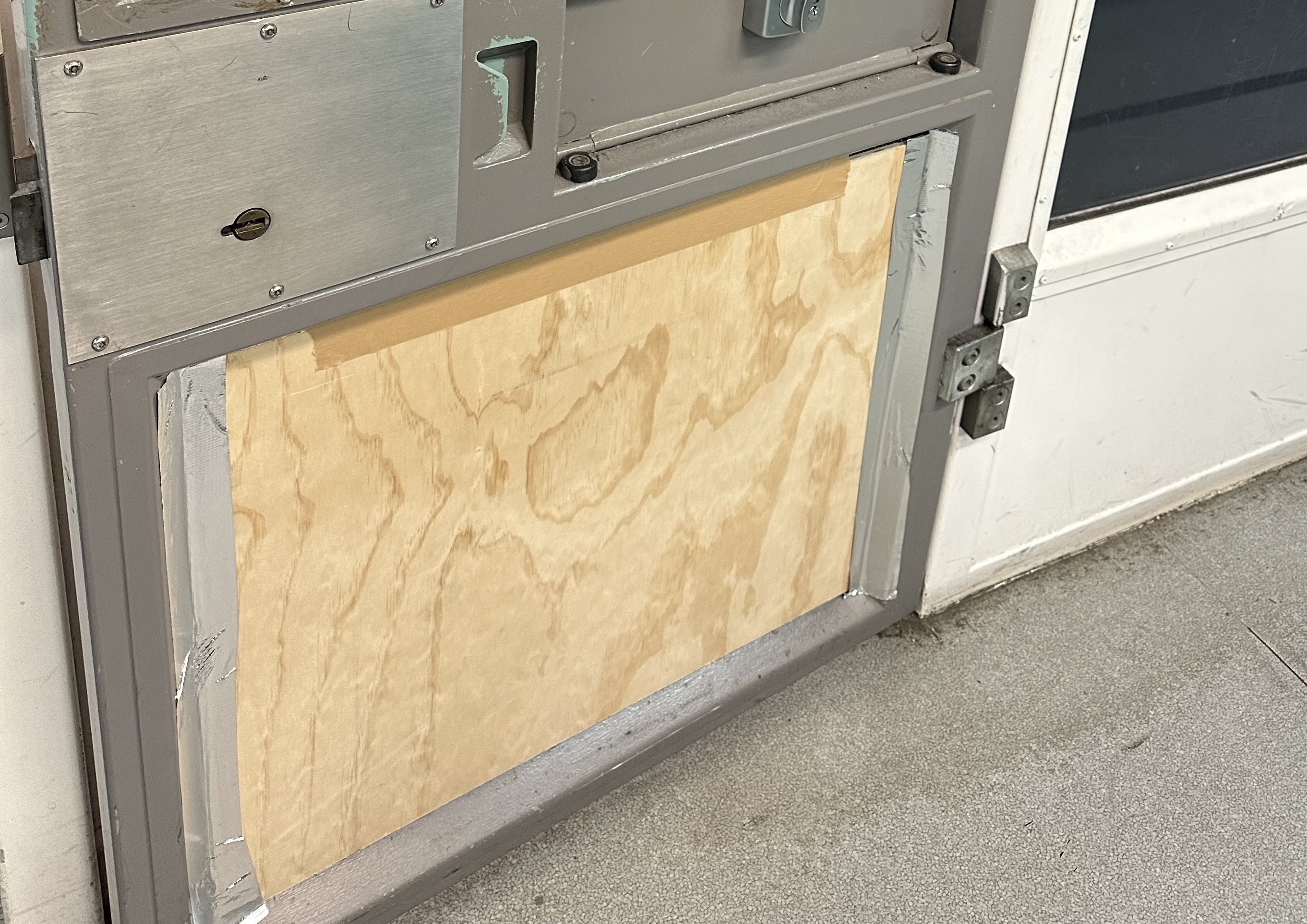 Plywood and tape cover the bottom section of a metal door.