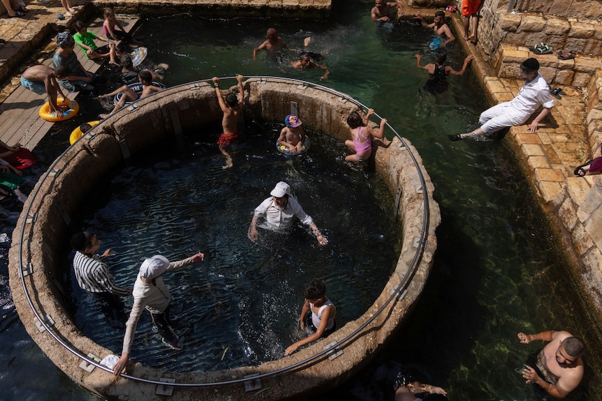 A top-down view of a group of people of varying ages and genders swimming in a man-made rocky pool.