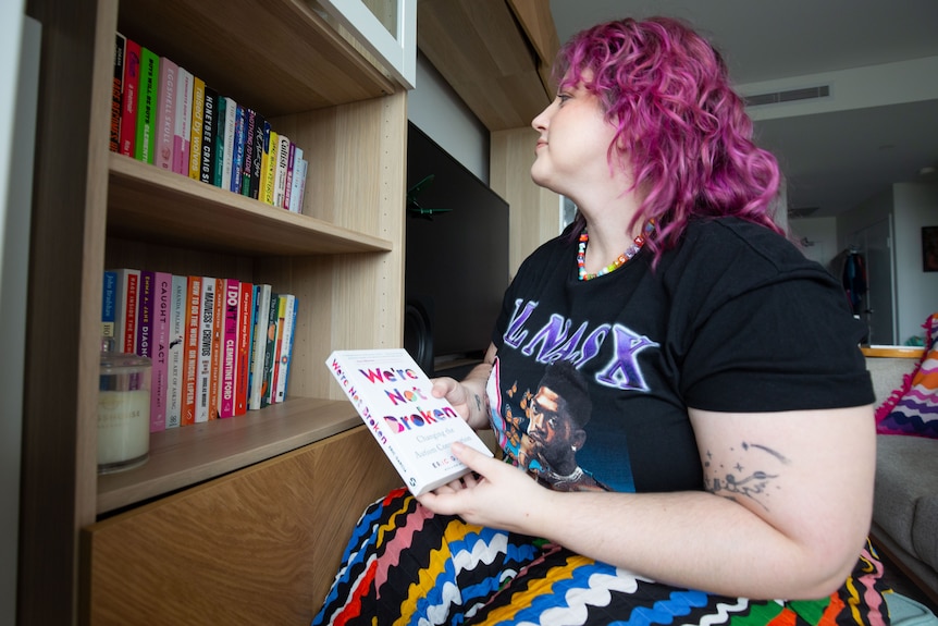 A person with pink hair and a colourful skirt in their apartment on a cloudy day