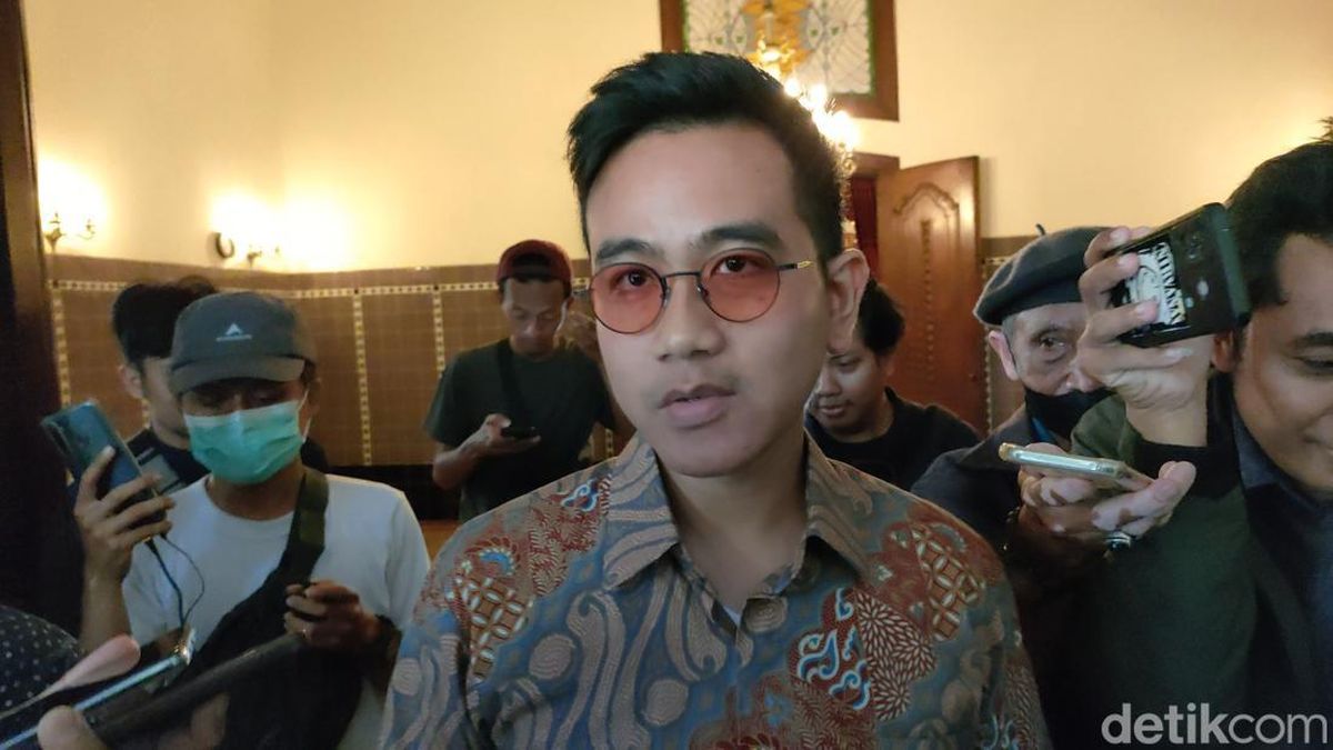 A man wearing a batik shirt, wearing glasses, in the middle of an interview with several media, facing the camera.