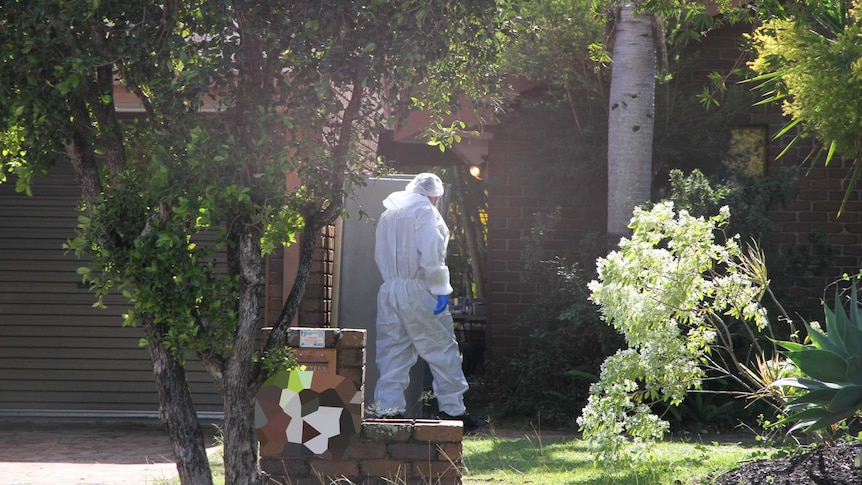 Forensic police officer wearing gloves and white body suit enters the home.
