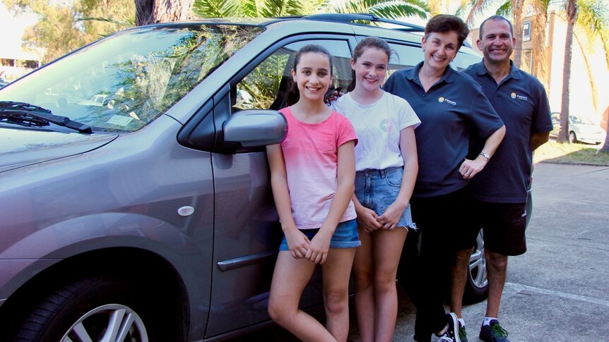 Two parents and their daughters outside a car