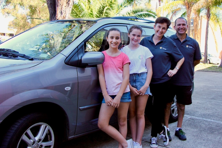 Two parents and their daughters outside a car