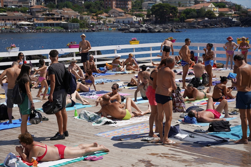 Люди стоят и лежат на полотенцах на палубе у океана в Италии. 