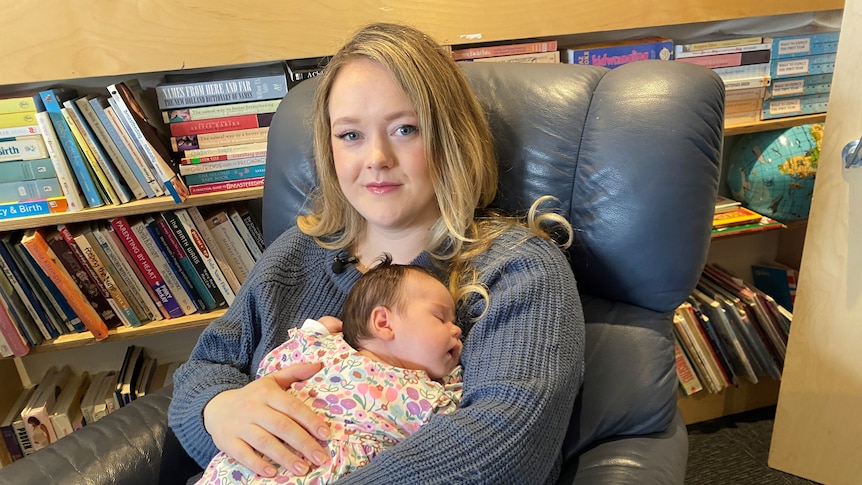 A woman sitting in an armchair holds a young baby.