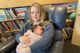 A woman sitting in an armchair holds a young baby.