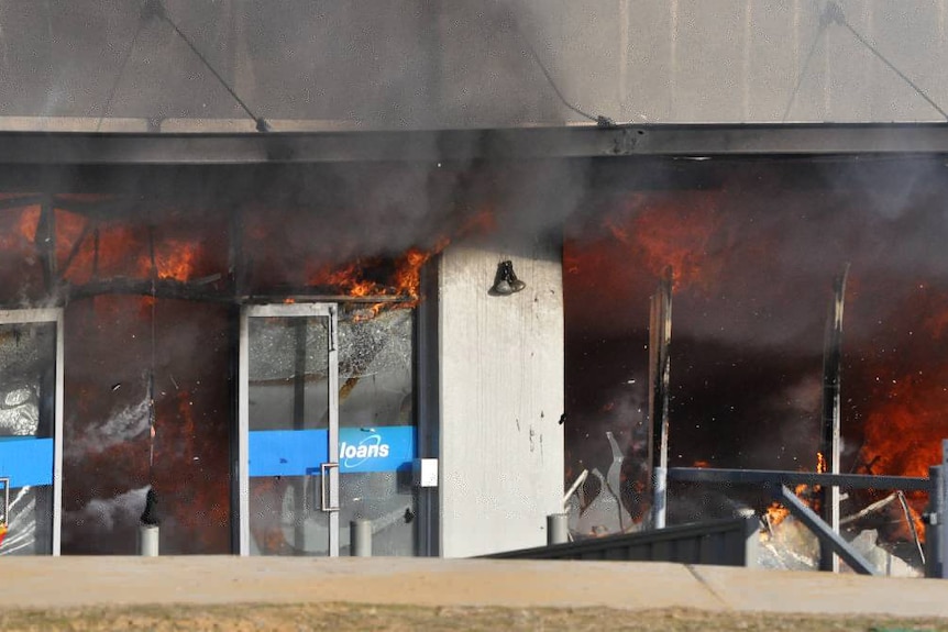 A close-up of flames engulfing the inside of a Cash Converters store, seen through the doors of the building.
