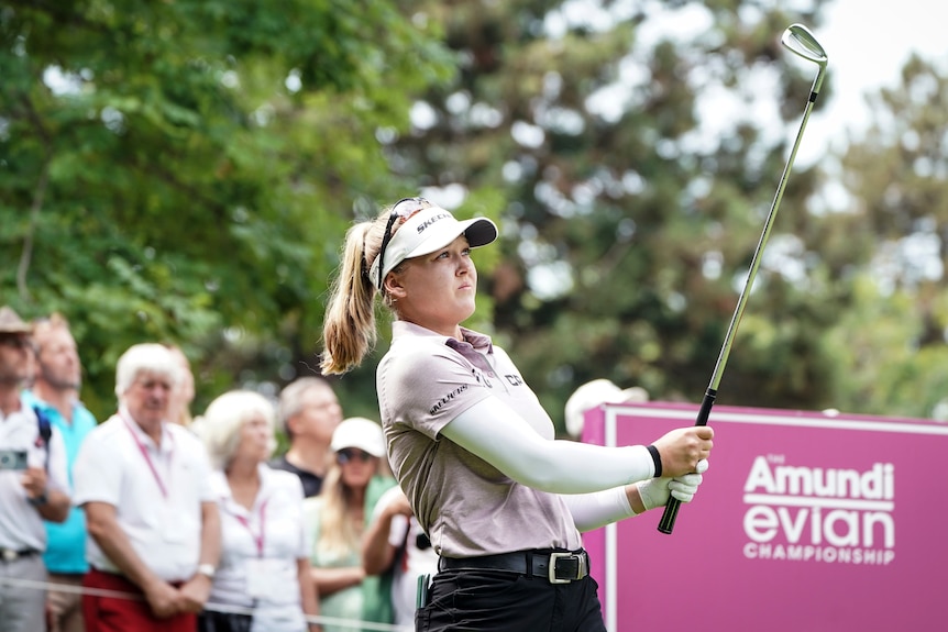Golfer Brooke Henderson holds her club at the end of her swing as she looks down the fairway watching her tee-shot.
