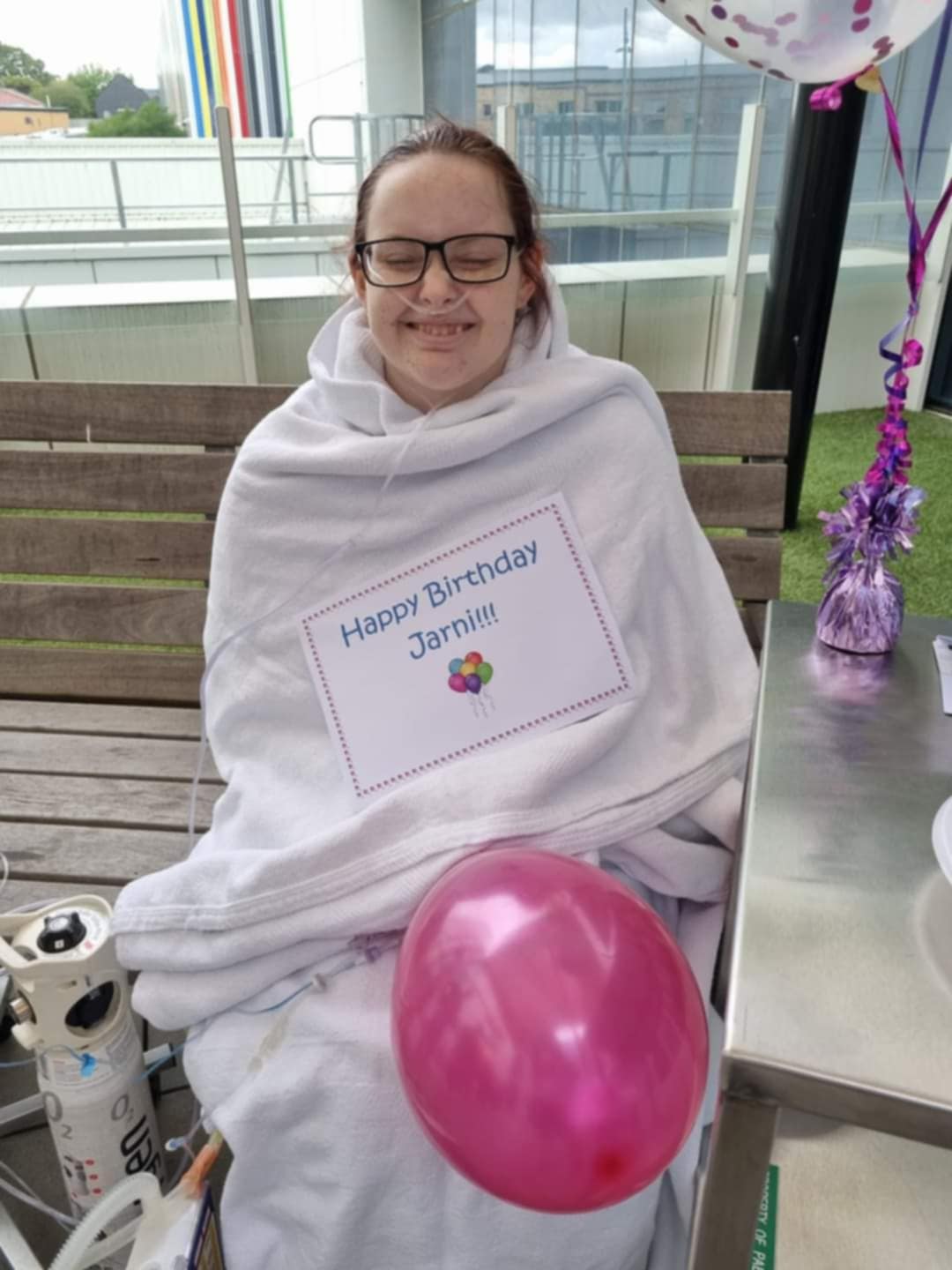 Jarni outside hospital with tubes and a happy birthday sign on her