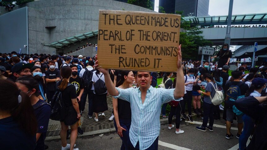 A man holds up a sign that reads "The Queen made us Pearl of the Orient. The Communists ruined it."