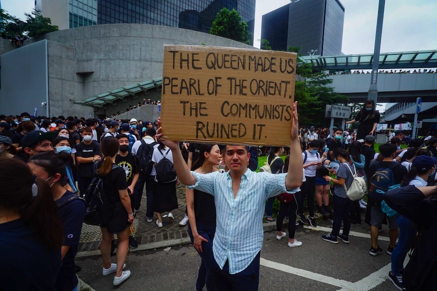 A man holds up a sign that reads "The Queen made us Pearl of the Orient. The Communists ruined it."