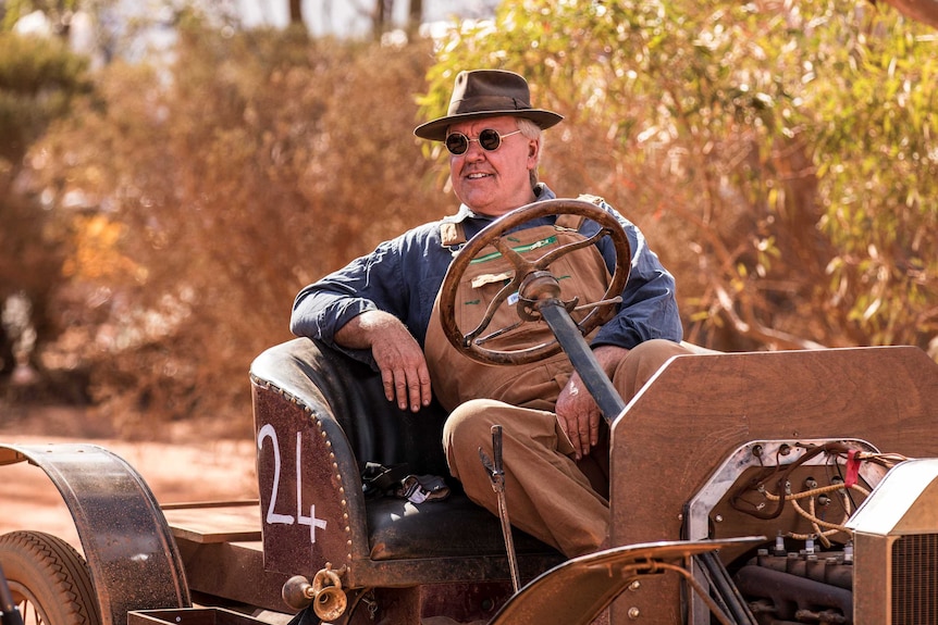 A man sits behind the wheel of a vintage car.