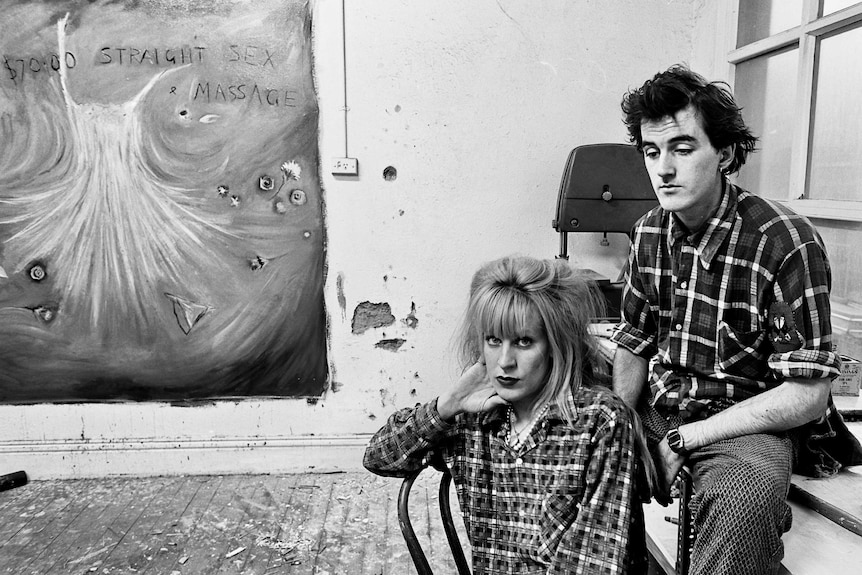 A black and white photo of a couple sitting with their arms around each other in an art studio