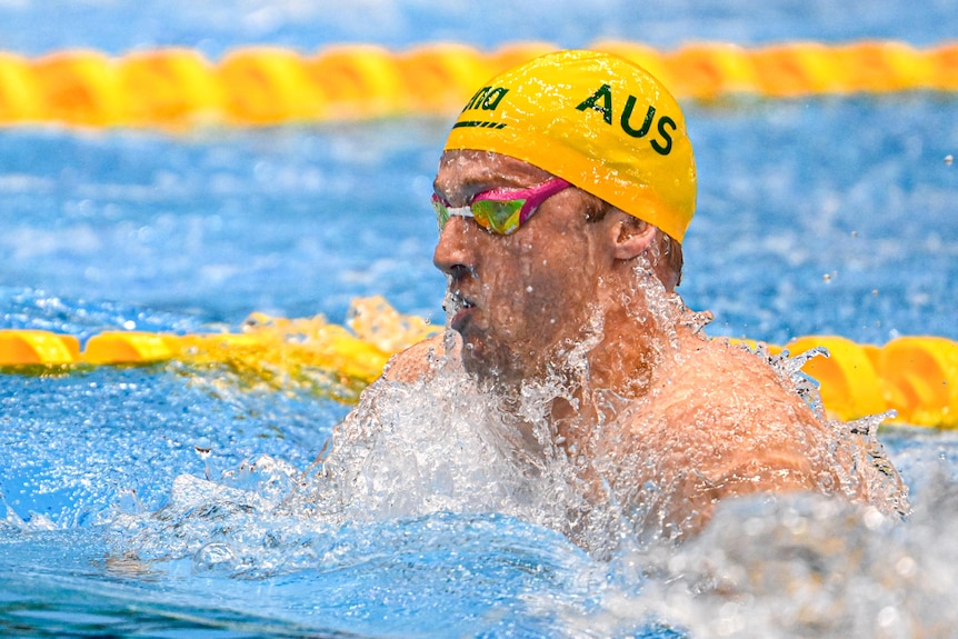 Sam Williamson bursts out of the water wearing an Australian gold swimming cap